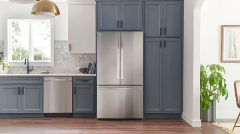 A stainless steel refrigerator with vertical doors on top and a bottom drawer freezer, mounted in blue cabinetry