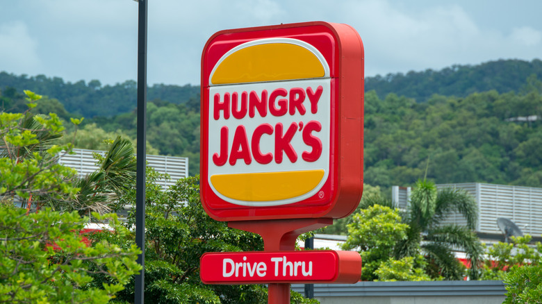 A Hungry Jack's burger-shaped sign in front of green hills