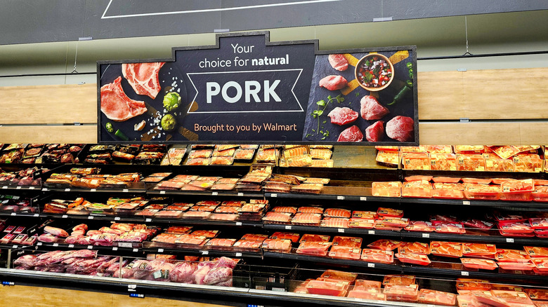 A walmart meat section with a large sign advertising pork hanging above the meat