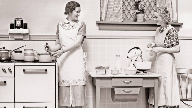 Two women smiling while doing housework in a kitchen