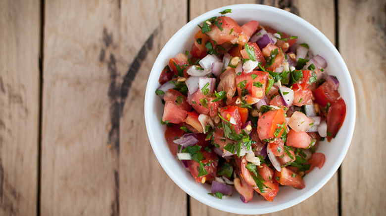 Pico de gallo with tomatoes, red onions, and cilantro in a white bowl on a wood slat tabletop
