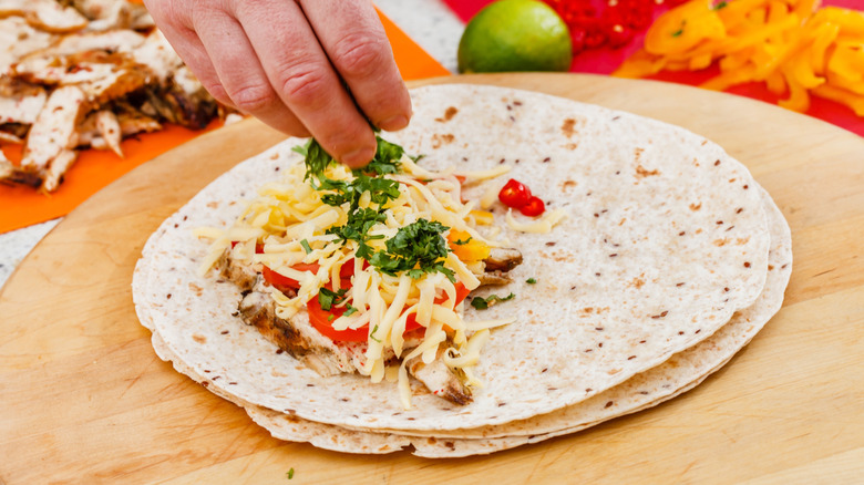 Hand adding cilantro to a tortilla with cheese, chicken, and other fillings to make a quesadilla