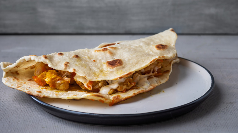 A small unsliced quesadilla on a white plate on a grey tabletop.