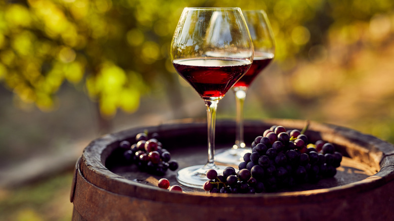 two glasses of red wine on barrel with bunches of grapes