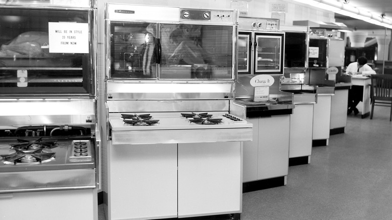 Black and white image of a vintage 1960s kitchen appliance showroom with ovens and stoves.