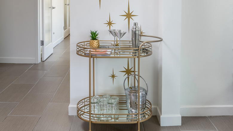 Vintage 1960s-style bar cart with bar accessories against a white wall and light floors