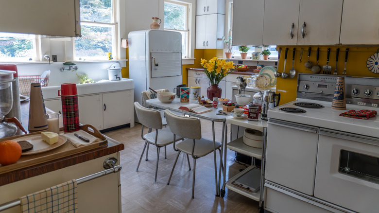 1960s kitchen with white counters, yellow walls, a white retro fridge, and white kitchen table.