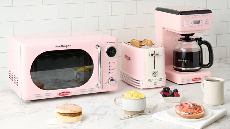 A suite of pink, vintage-style Nostalgia kitchen appliance products on a counter.