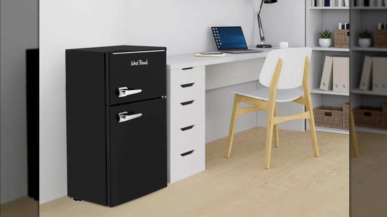 A black vintage mini fridge by West Bend sitting in an office room.