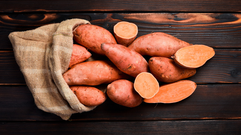 Sweet potatoes spilling out of a sack on a dark wooden table
