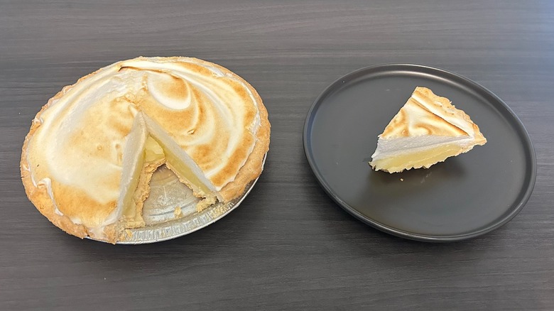 Freshness Guaranteed lemon meringue pie with slice missing and slice on a black plate