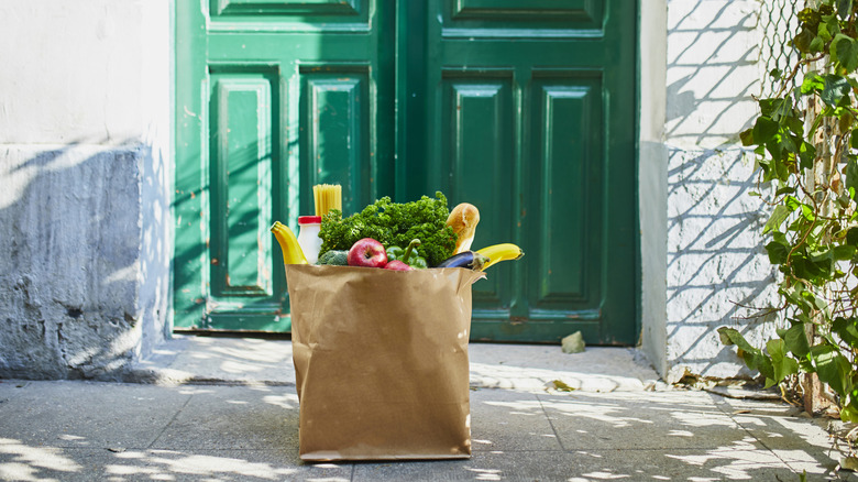 A brown paper bag full of groceries sitting outside someone's front door