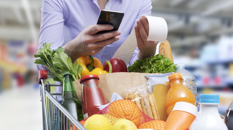 A person checking a receipt with a cart full of groceries