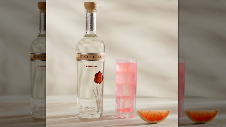 Bottle of Excellia Blanco next to a pink cocktail in a glass