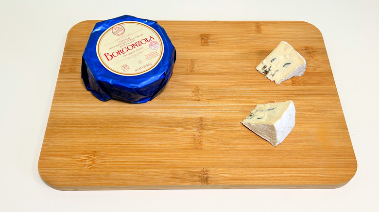 Pieces of cheese on a cutting board next to a package of Emporium Selection Borgonzola