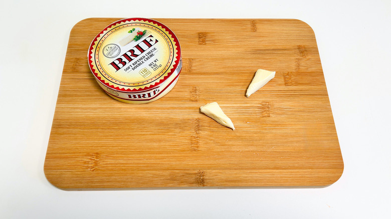 Pieces of cheese on a cutting board next to a container of Emporium Selection Double Creme Brie