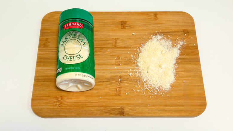 Grated cheese on a cutting board next to a bottle of Reggano Grated Parmesan Cheese