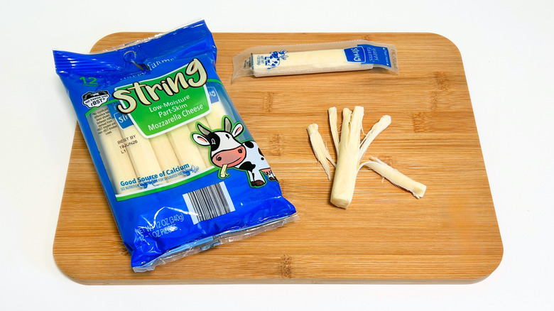 Pieces of cheese on a cutting board next to a bag of Happy Farms Part-Skim Mozzarella String Cheese