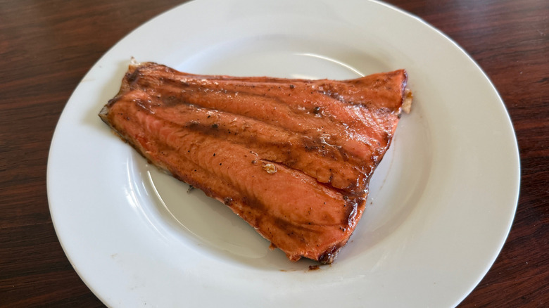 A piece of cooked trout with a barbecue sauce glaze on a white plate