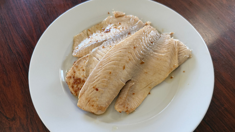 Two cooked tilapia fillets on a white plate