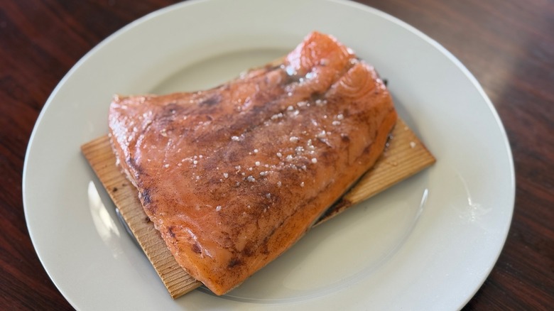 A piece of honey-maple glazed salmon on a wood plank on a white plate