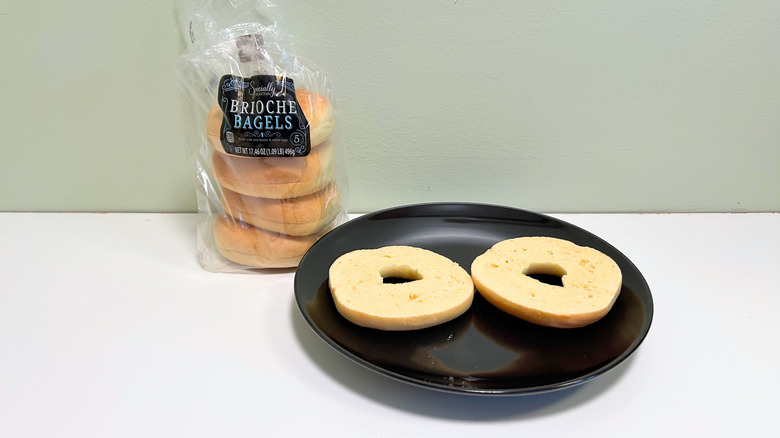 A bag of Specially Selected Brioche Bagels next to a black plate with a sliced bagel
