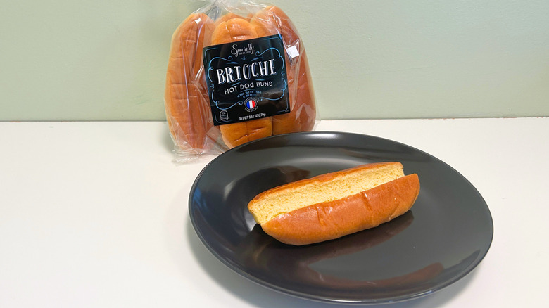 A bag of Specially Selected Brioche Hot Dog Buns next to a black plate with a hot dog bun