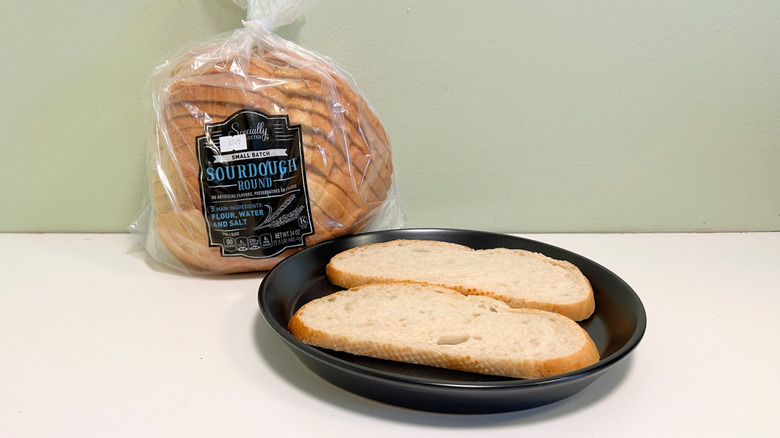 A bag of Specially Selected Small Batch Sourdough Round next to a black plate with bread slices