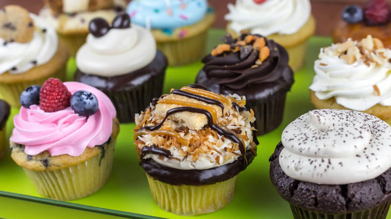 A green tray of several colorful cupcakes in different colors