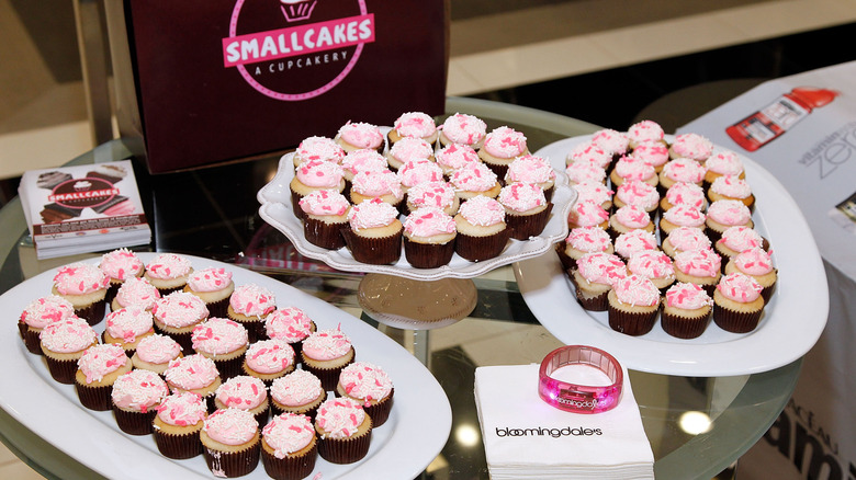 Three plates full of pink Smallcakes cupcakes on a glass table at a Bloomingdales event