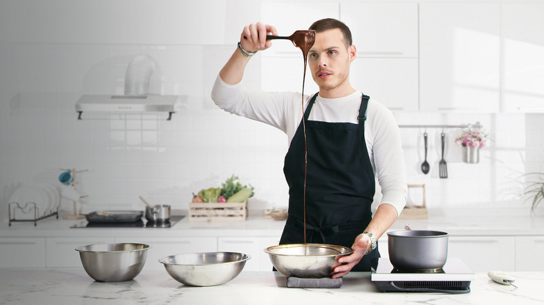 Chef Amaury Guichon holding a spatula with chocolate dripping off it into a steel bowl