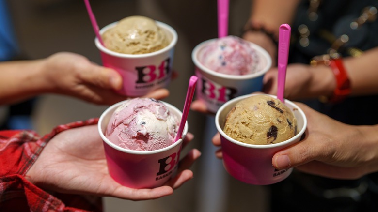 Four hands each holding one scoop of Baskin-Robbins ice cream in cups