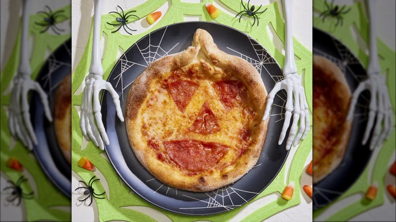A personal pizza with large pepperonis and a twist in the crust to resemble a jack-o'-lantern
