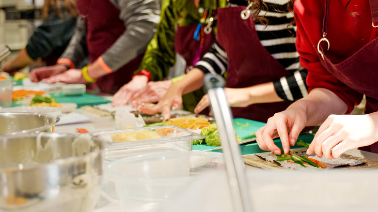 A line of amateur cooks all preparing sushi rolls