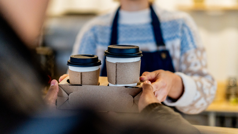 A customer accepting a take-out coffee order from a barista