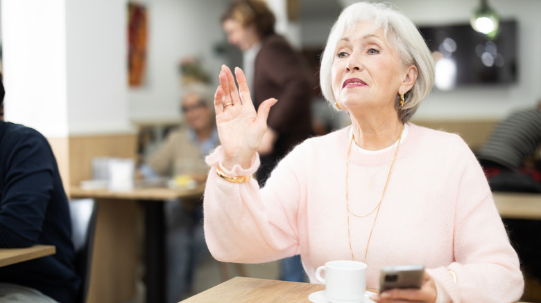 A senior woman trying to get a server's attention at a coffee shop