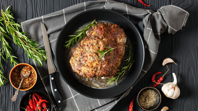 A piece of cooked meat in a black cast iron pan with rosemary and chilis