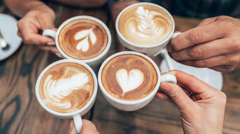 Four people raise their coffee mugs with latte art in a cheers