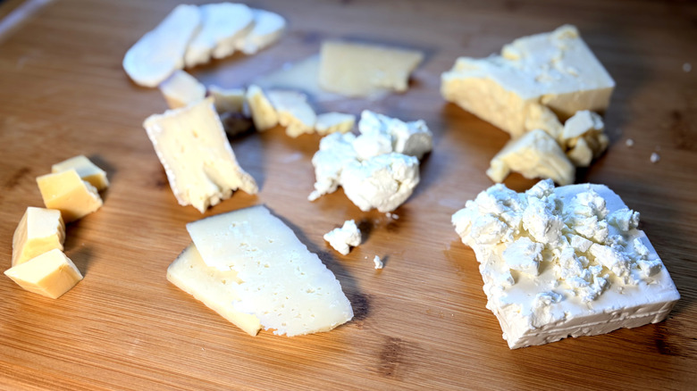Various cheeses sliced or crumbled on a cutting board