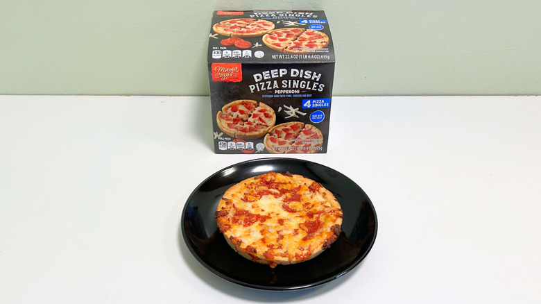 A box of Mama Cozzi's Pepperoni Deep Dish Pizza Singles next to a black plate of deep dish pizza