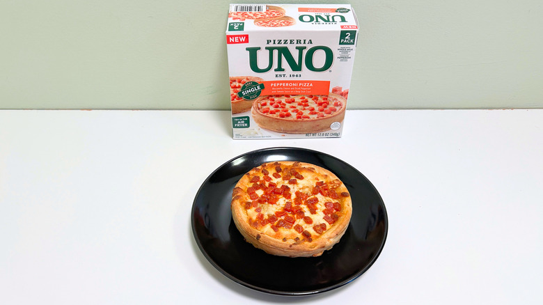 A box of Pizzeria Uno Pepperoni Deep Dish Pizza next to a black plate of deep dish pizza