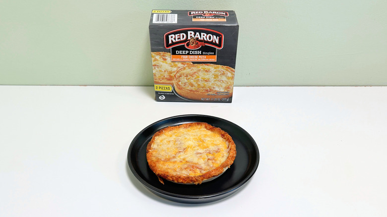 A box of Red Baron Four Cheese Deep Dish Pizza next to a black plate of deep dish pizza