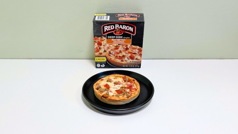 A box of Red Baron Meat-Trio Deep Dish Pizza Singles next to a black plate of deep dish pizza