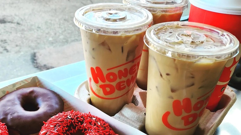 Four coffees in a tray next to box of donuts
