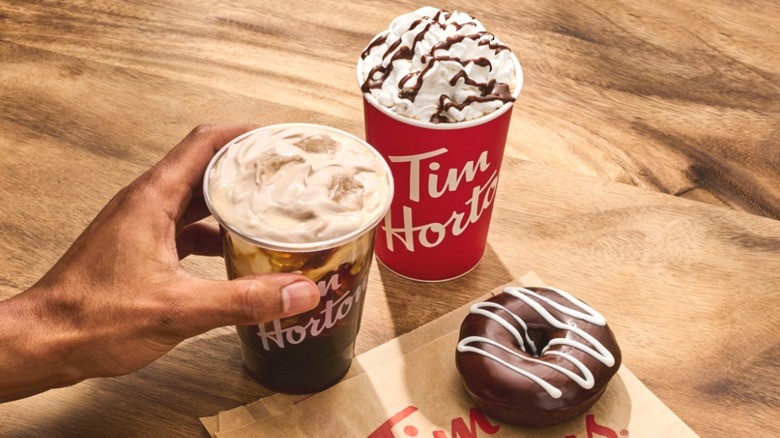 Hand placing iced coffee on table with hot drink & donut