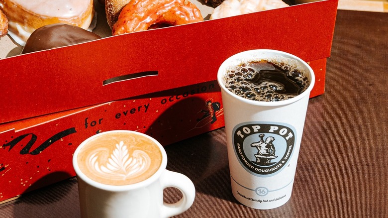 Two hot coffees placed in front of an open box of donuts