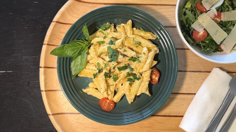 Beecher's Mac & Cheese on a plate on with basil next to an arugula salad, fork, and knife