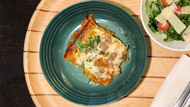 Kirkland Beef & Italian Sausage Lasagna on a plate on with basil next to an arugula salad, fork, and knife