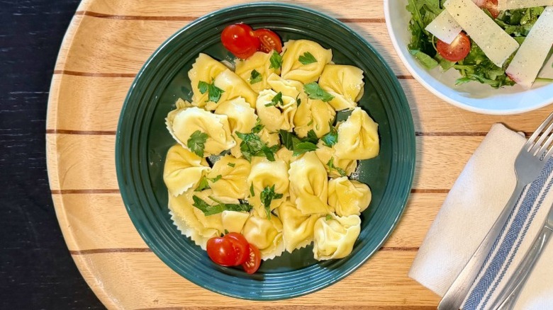 Kirkland Five Cheese Tortelloni on a plate on with basil next to an arugula salad, fork, and knife