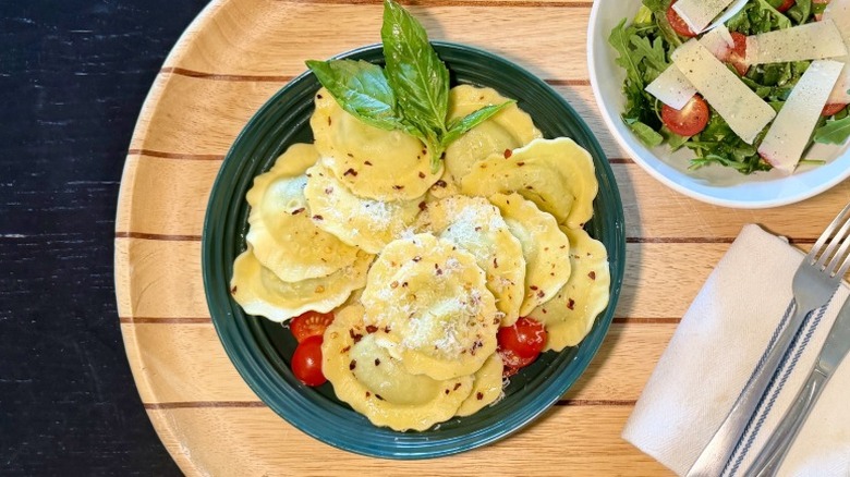 Kirkland Spinach & Cheese Ravioli on a plate on with basil next to an arugula salad, fork, and knife